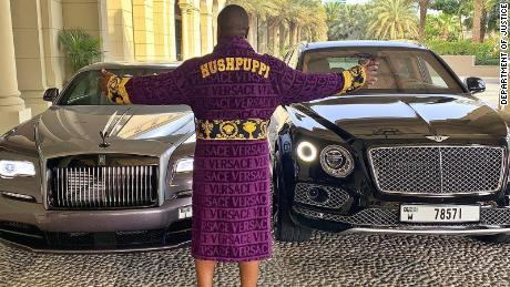 A social media influencer known as "Hushpuppi" poses with two luxury cars.