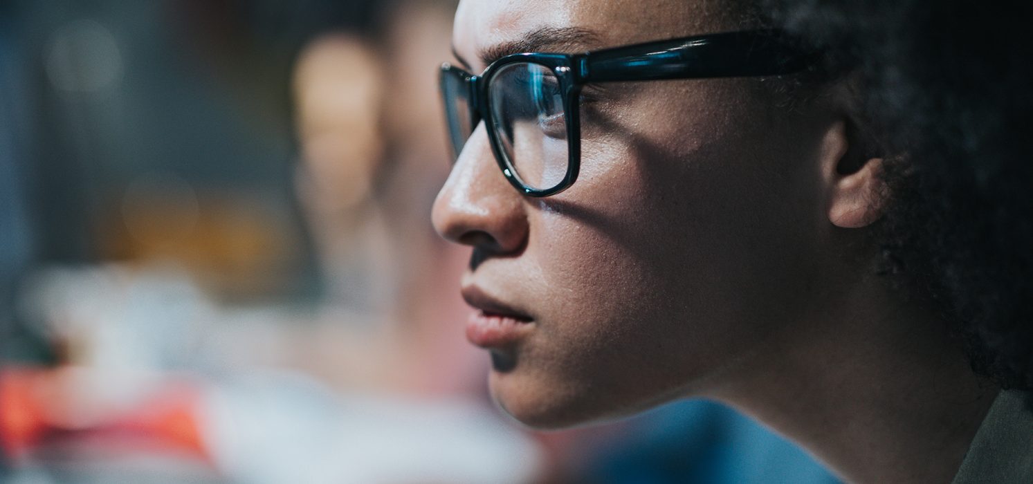 Close-up side profile of a Black woman wearing glasses, focused intently on something out of frame.