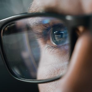 Pictorial representation of attack surface management. Close-up of a person wearing glasses with computer code reflections on the lenses.