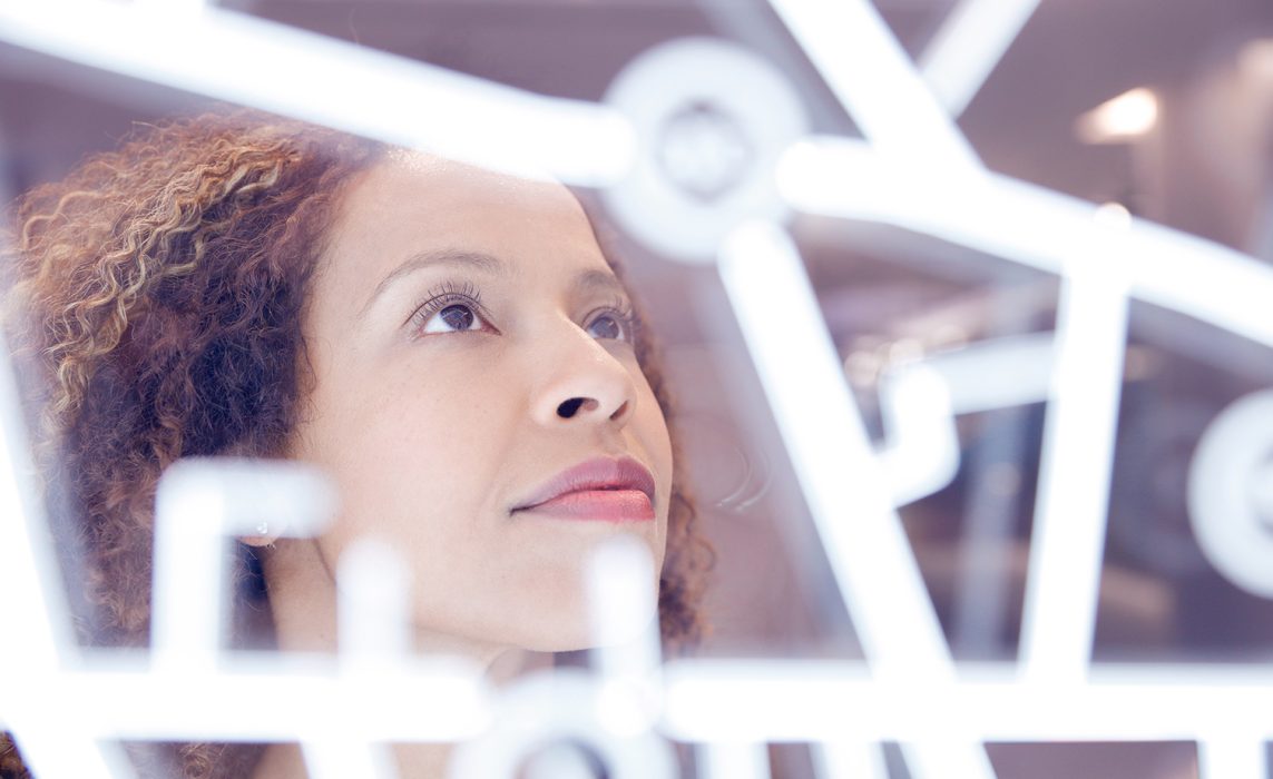 Pictorial representation of a woman analyzing a bright, white characters on a clear screen.