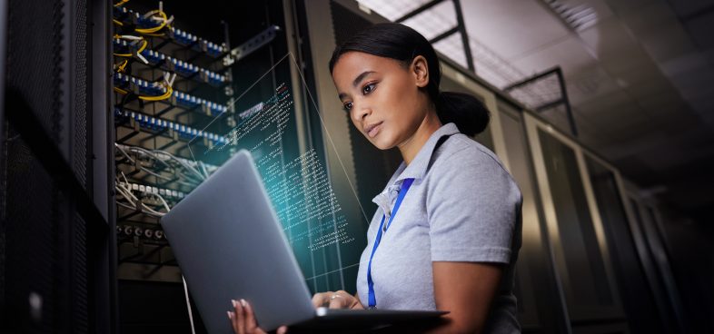 Pictorial representation of a woman standing in a server room holding a laptop that projects a digital code overlay.