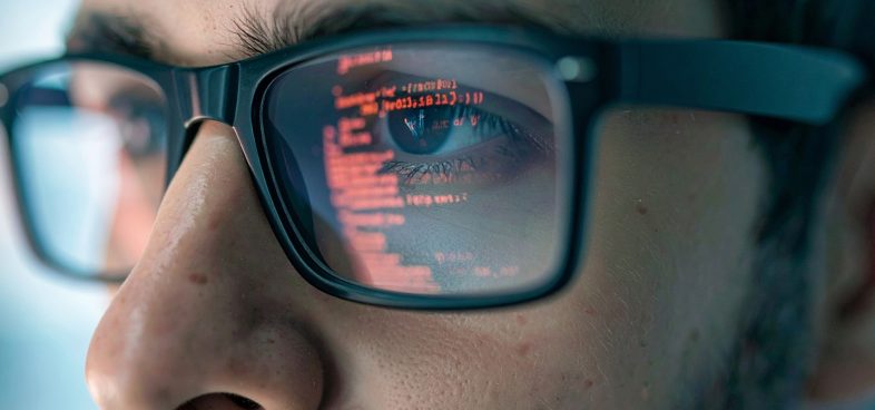 Pictorial representation of WebAuthn. A person wearing glasses with computer code reflected in the lenses. The focus is on the eye, and the code is clear and detailed.
