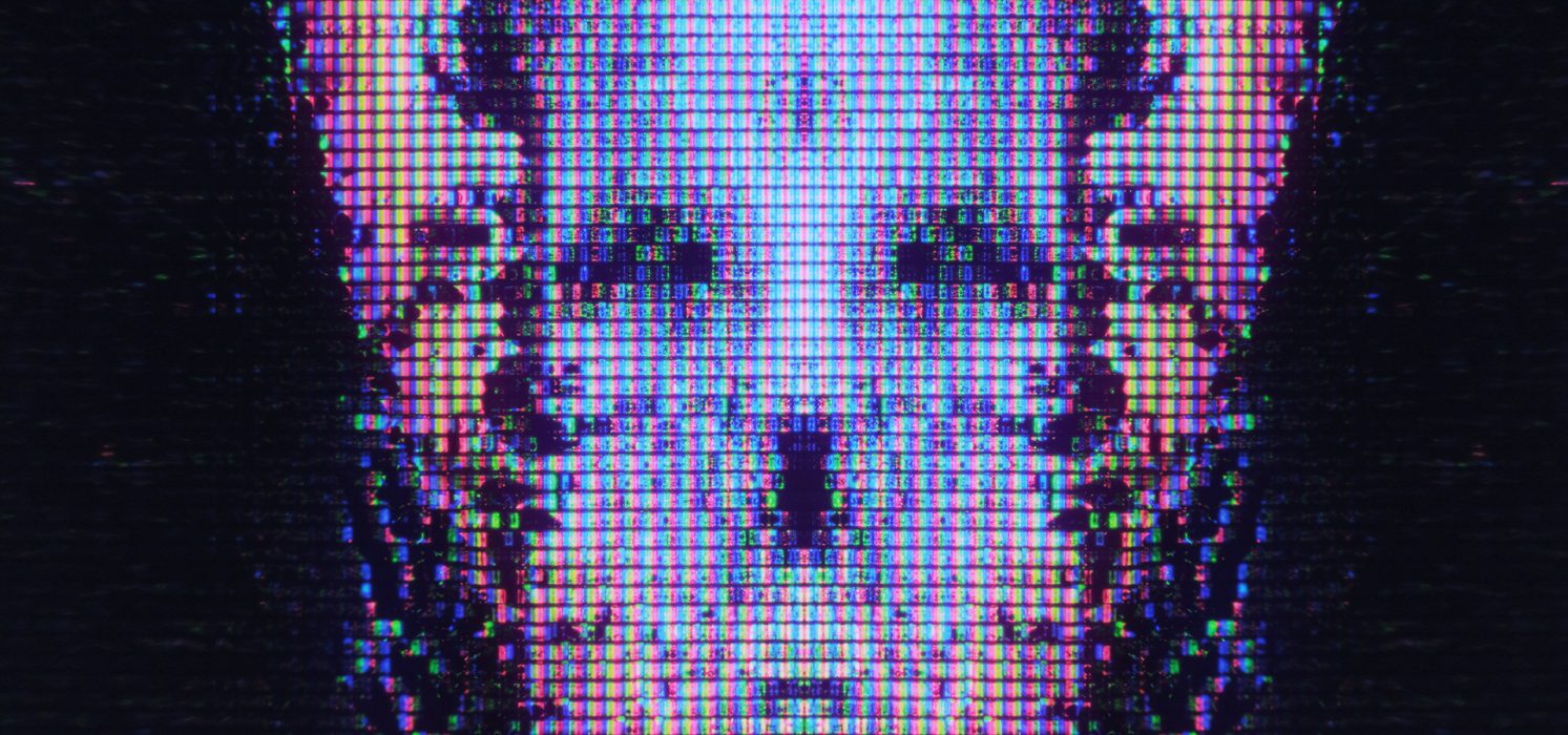 Pictorial representation of identity abuse through trusted communication channels. Close-up view of a digital screen displaying a glitched and pixelated image of a skull-like shape.